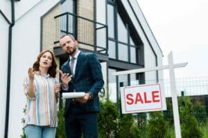Woman and man standing in front of a 'For Sale' house sign