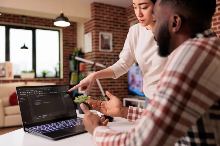 Digital Marketing Agency A woman points at a laptop screen with code on it while a man sits beside her, discussing the content in a modern office setting. Paradox Media
